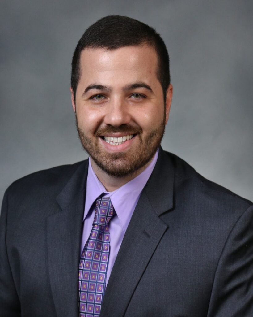Smiling man in suit and purple tie.